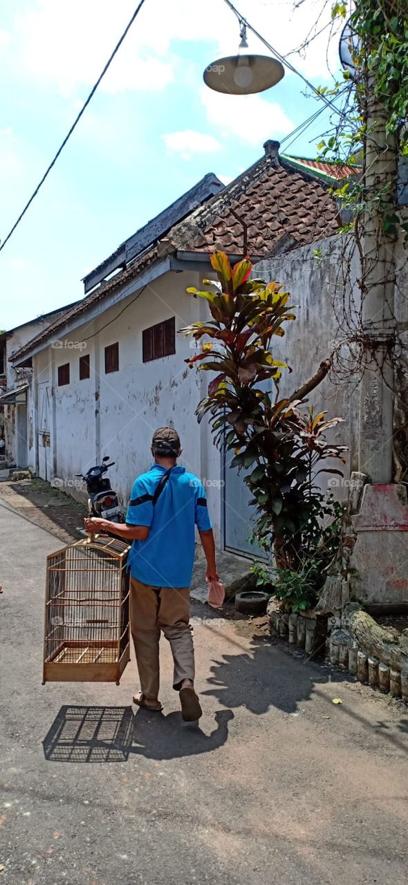 a man is walking while carrying a  birdcage