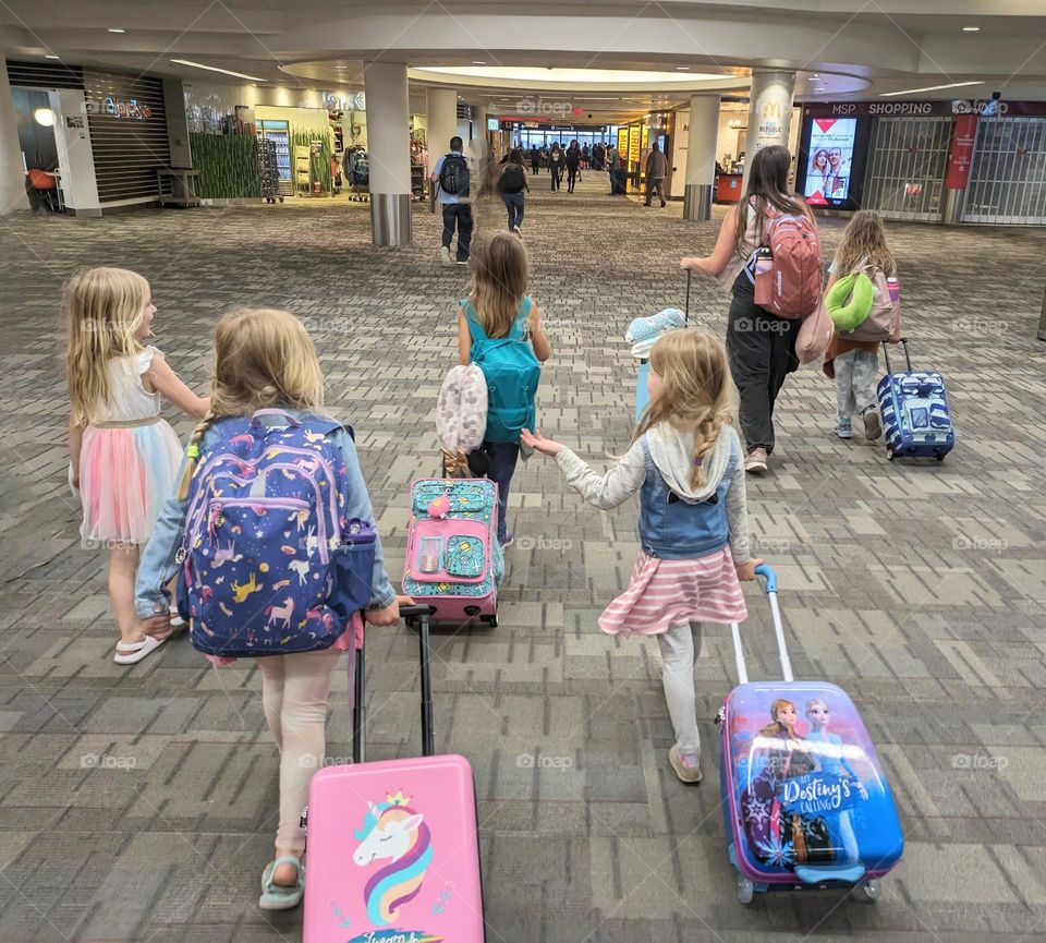 5 little girls wheeling their luggage together through the airport excited for their flight together, cute luggage and girly backpacks