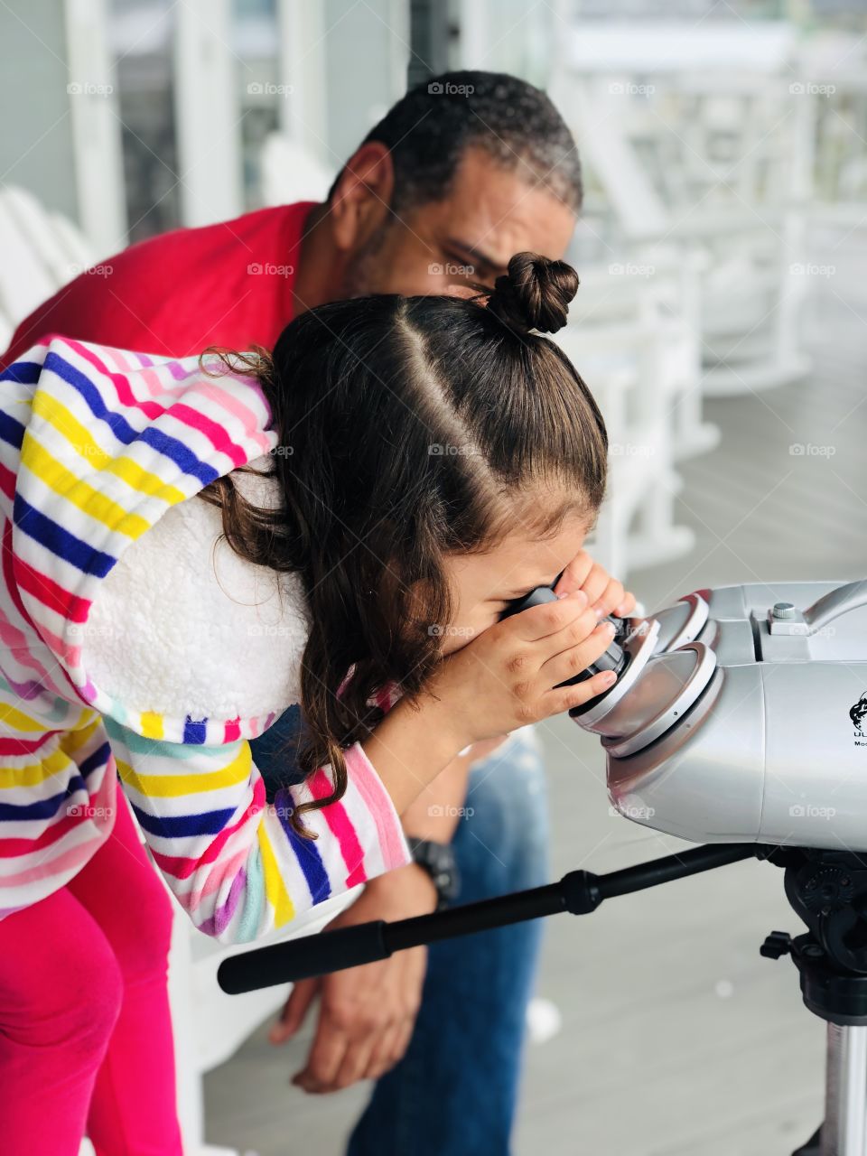 Child standing with man while using binoculars to look at the beach