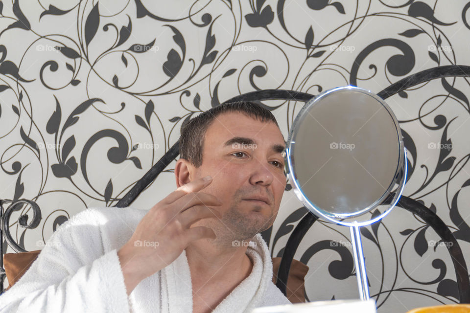 A man and home spa care at home takes care of himself and smears his face with cream, does a manicure at home on a blue background and with oranges and rests.