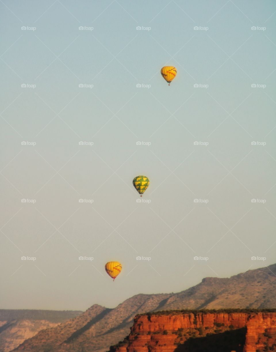 three hot air balloons flying on the top of the mountain during sunrise at Sedona