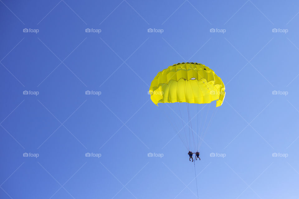 Yellow parachute with two people flies in the blue sky
