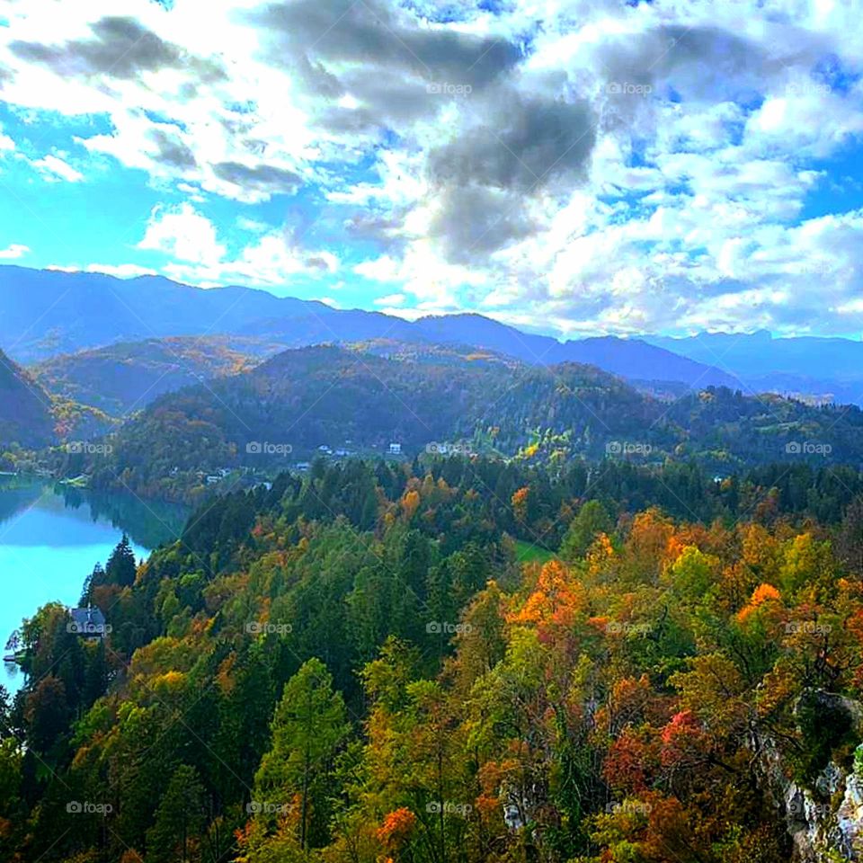 Forest. The blue lake is surrounded by forested mountains. Forest in autumn. Above the autumn trees gray clouds through which the sun breaks