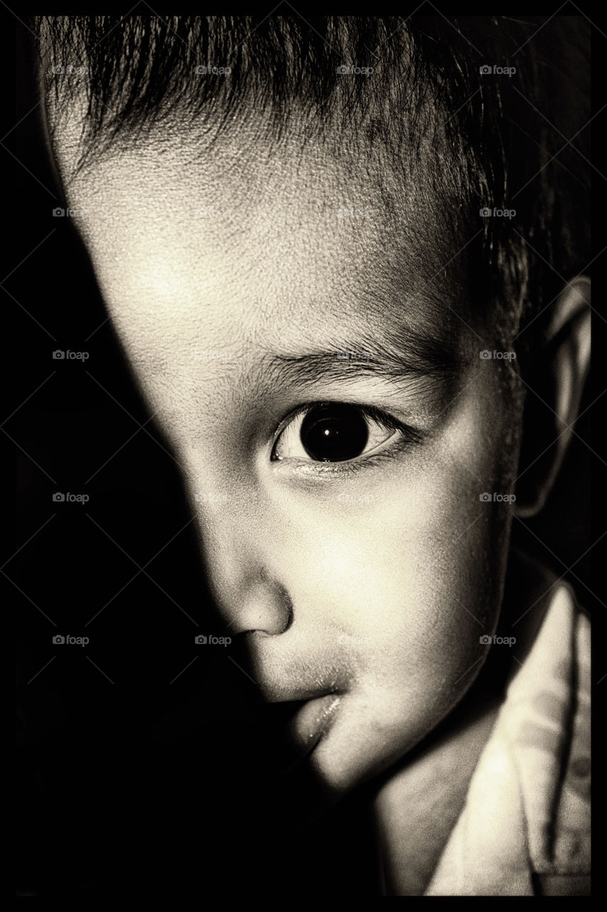 Cute boy hiding behind curtain. Caught my son Thithi playing hide and seek, he was hiding behind a curtain, the light was low,no flash and the result is a portrait half covered by the shadow