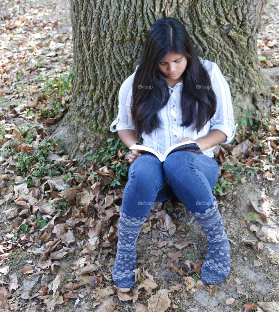 Girl reading a book while sitting under a tree