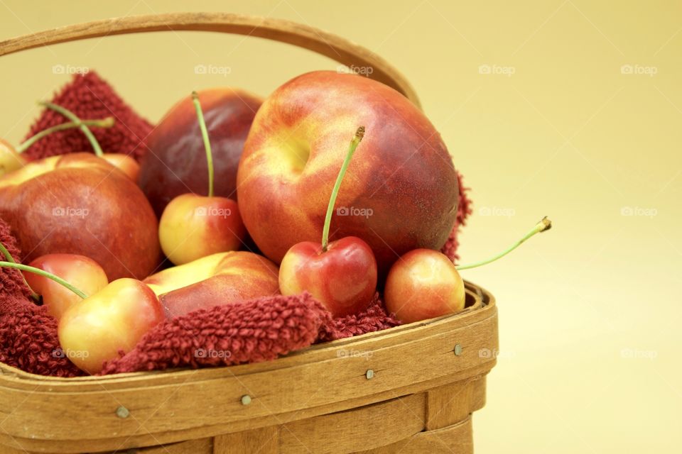 Fruits! - Nectarines And Rainer cherries in a wooden basket against a yellow background 