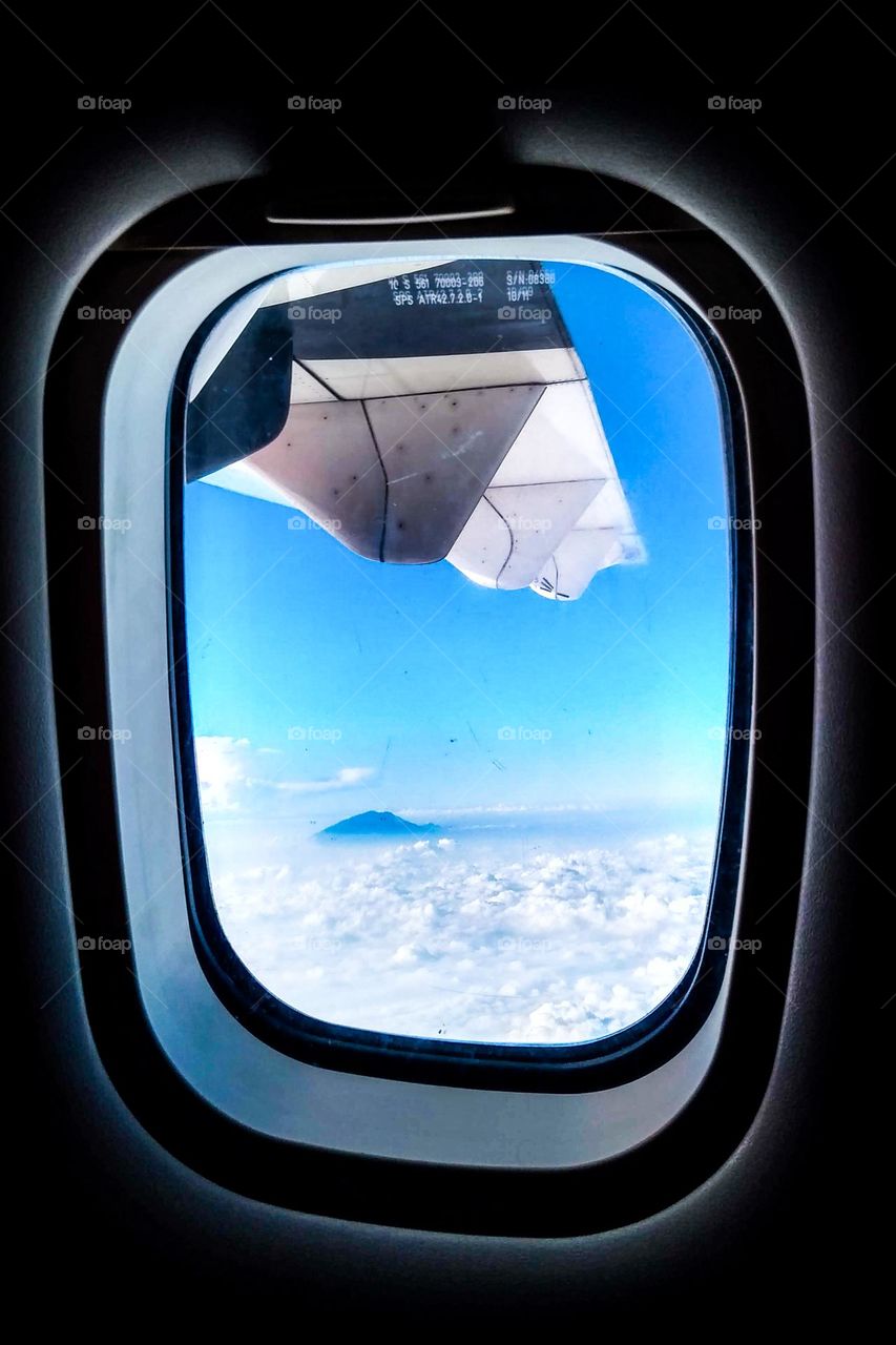 From behind the plane window you can see the sky and clouds below at eye level view