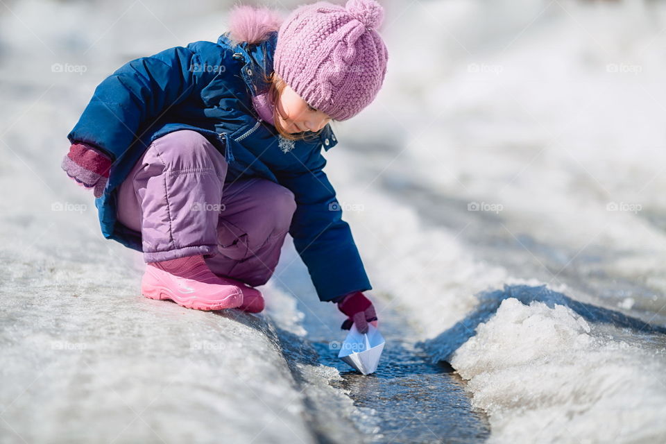 Little girl with paper boat on creek 