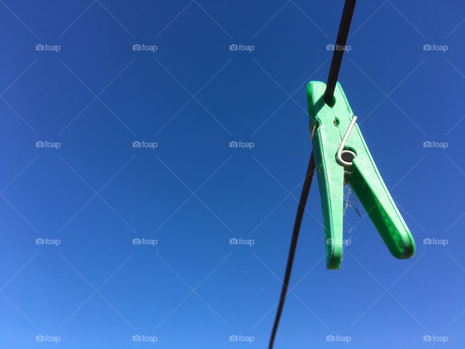 Vivid colour accentuated here by bright green plastic clothespin clothes peg hanging on clothesline against a clear blue sky with plenty of room for copy or text 