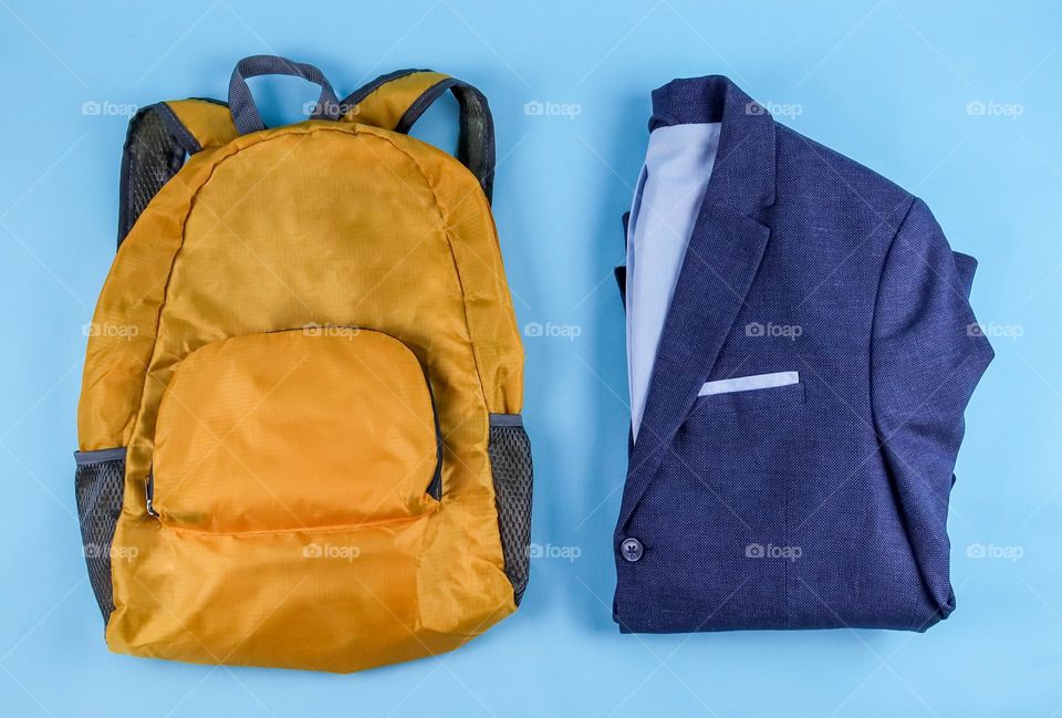 One yellow backpack and a folded blue men's jacket lie on a light blue background, flat lay close-up. Concept back to school, business trip.