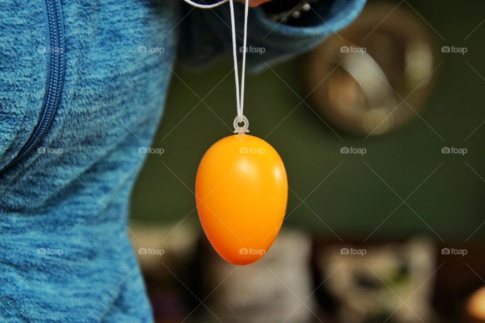 Close-up of a yellow hanging Easter egg in living room held by a woman 