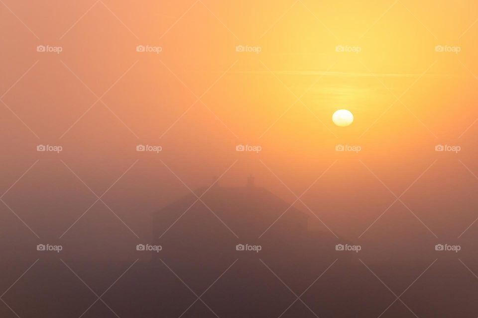 A calm and foggy sunrise. I just love the way you see the silhouette of the house, and the warm orange colors from the sun.