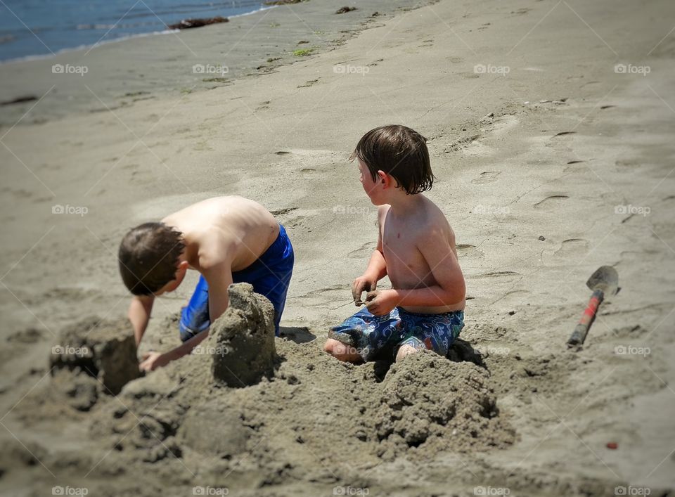 Young Boys At The Beach. Two Young Brothers Building A Sandcastle
