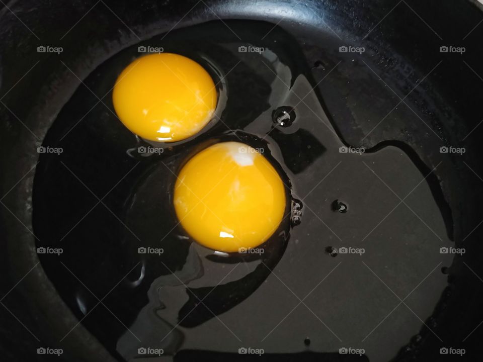Two raw eggs with a bright yellow/orange yolks and clear egg whites sitting in a shiny, black cast iron skillet.