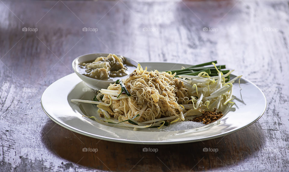 Fried noodle with spring onion and bean sprouts on white plate with garnish.