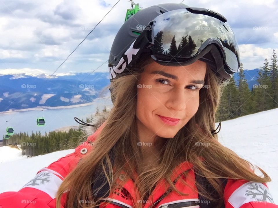 Portrait of woman skier wearing Uvex ski glasses and Uvex helmet with ski lifts in the background 