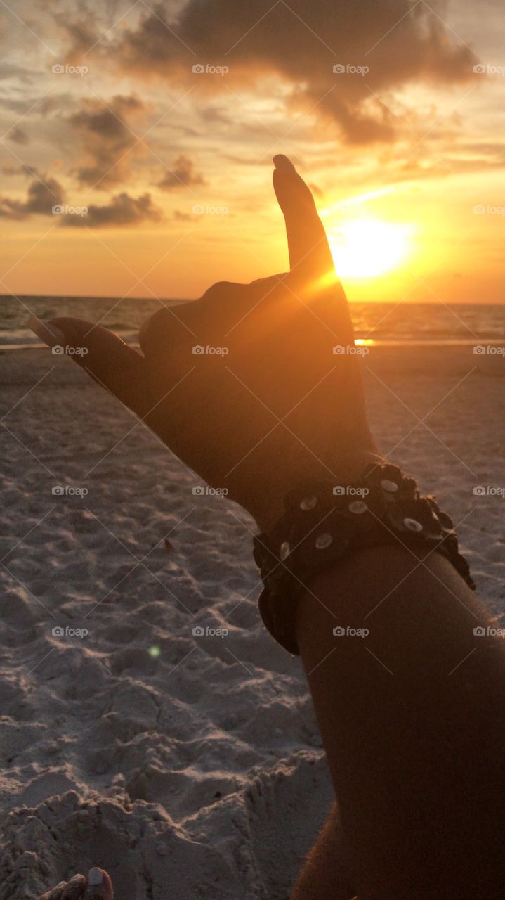Shaka in the sunset. Salute to the beautiful sunset in the Gulf of Mexico beach. St Pete Beach, Florida. White nails, leather bracelet, tan. Fun and relaxing.