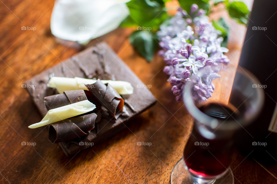 Beautiful chocolate lovers lifestyle gourmet food and wine photography pairing dark chocolate with wine next to glass of port on desktop with fresh lilac flowers and rose petals 