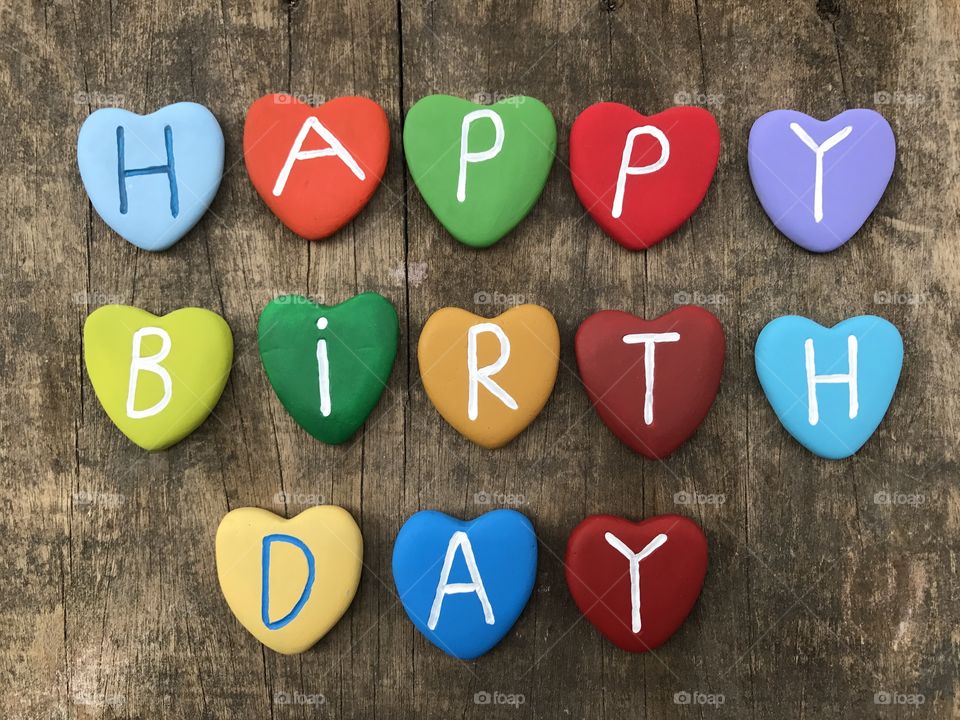 Happy Birthday message with multicolored heart stone letters over wooden raw board