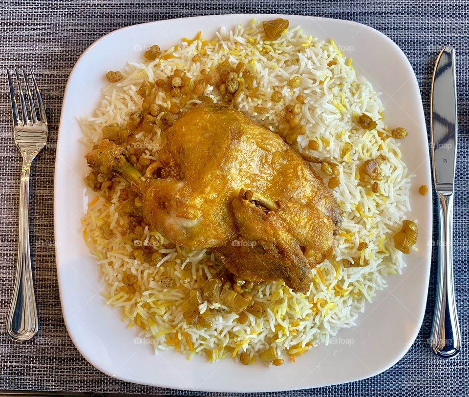 Delicious kuwaiti authentic Chicken Majbous meal with rice and saffron is on white plate next to knife and fork