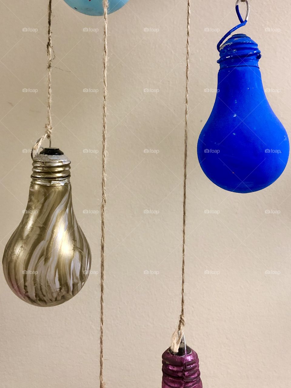 Arts and crafts project of painted light bulbs suspended by twine against interior wall 