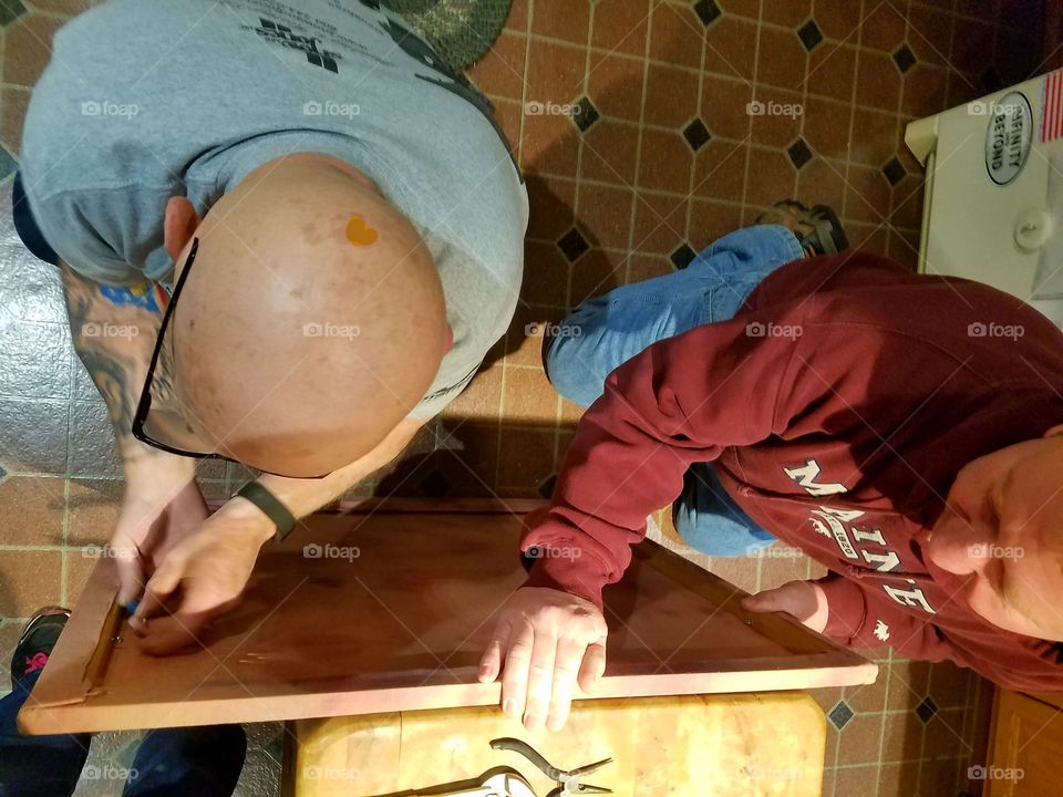 Two men putting hangers onto back of frame to hang wall hanging on wall. Good job guys!