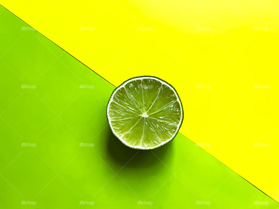 Slice of green lime on yellow and green background 