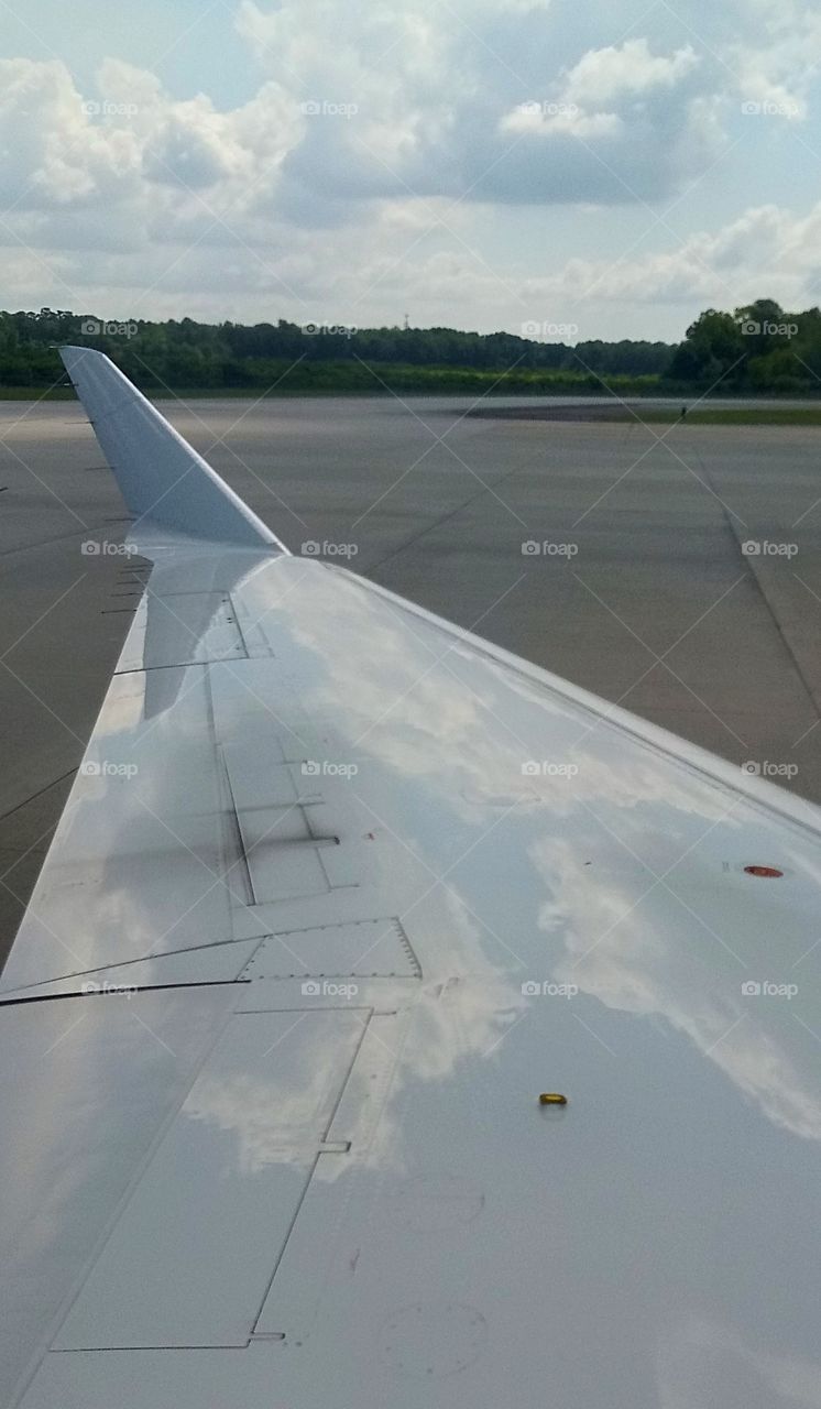an airplane wing reflecting a partially cloudy sky
