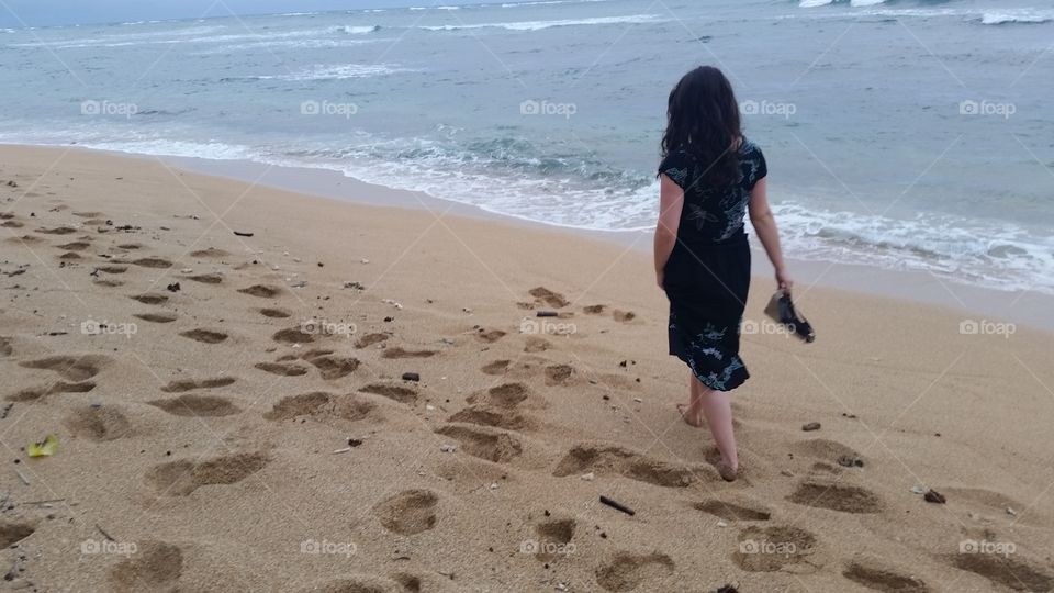 Woman walking on sandy beach, ocean Shoreline in Kauai, Hawaii on sunny day on vacation