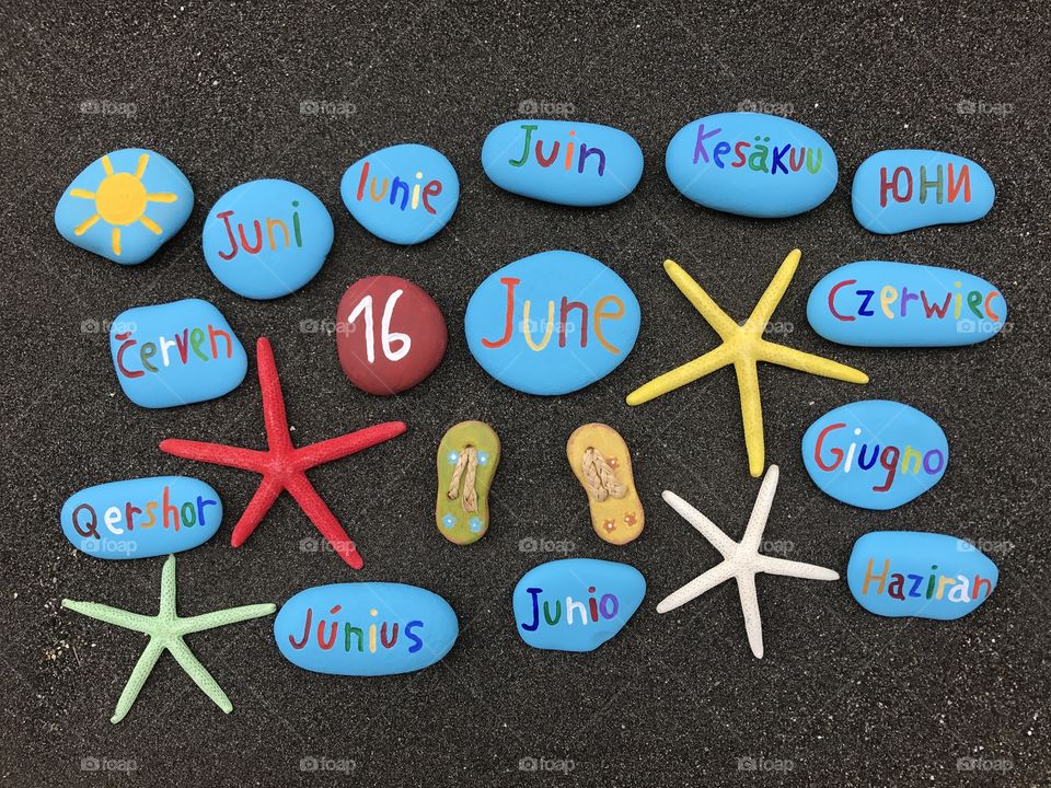 16 June, calendar date with multicolored stones and starfishes over black volcanic sand