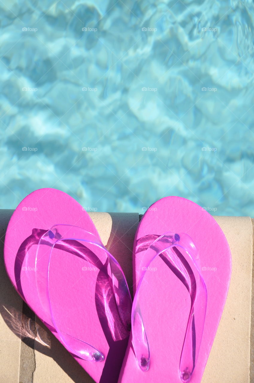 Pink flip flops sitting by the pool. 