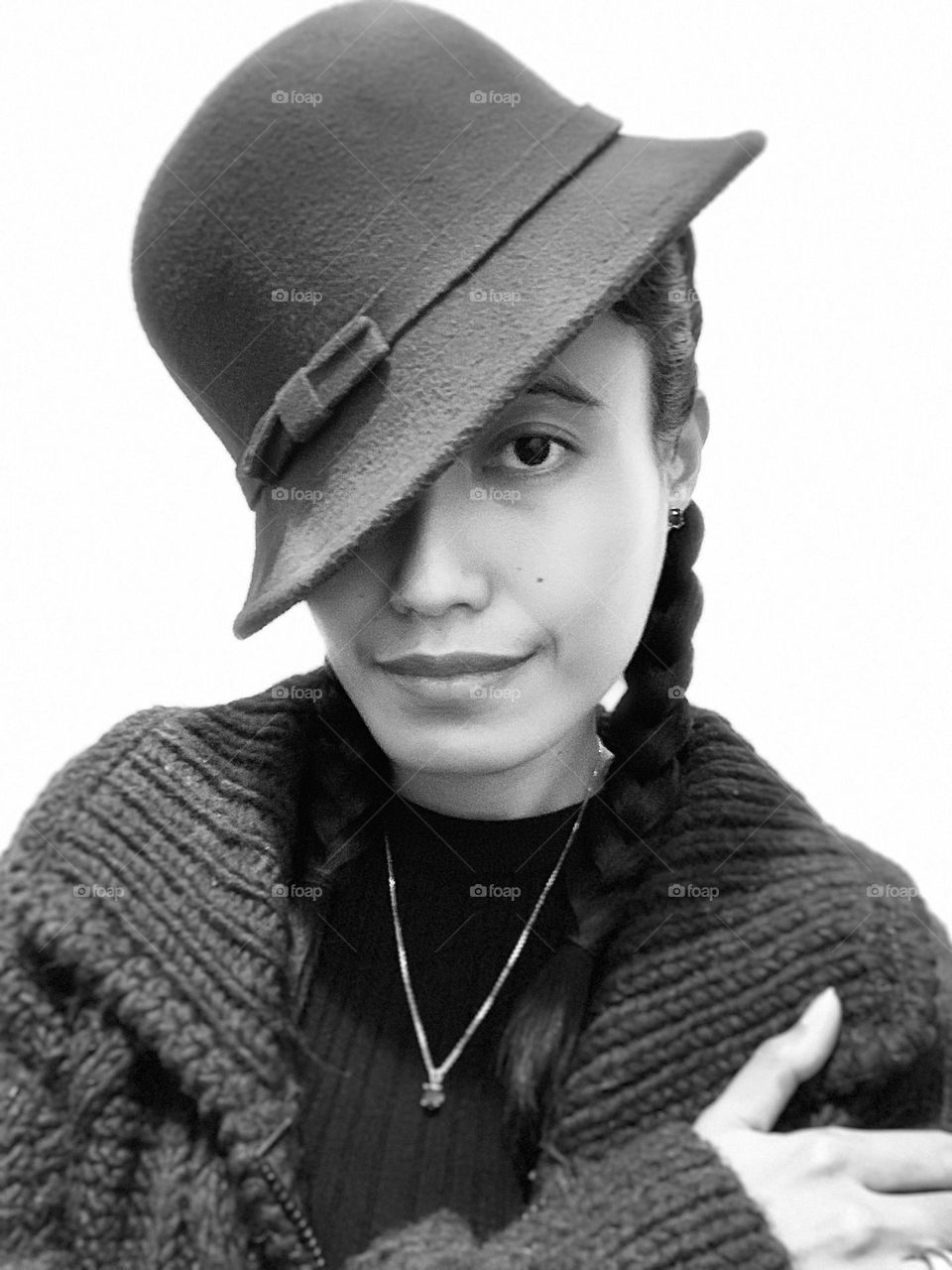 A woman wearing a a fashion hat. One eye is covered by the hat. Braided hair. Black and white.