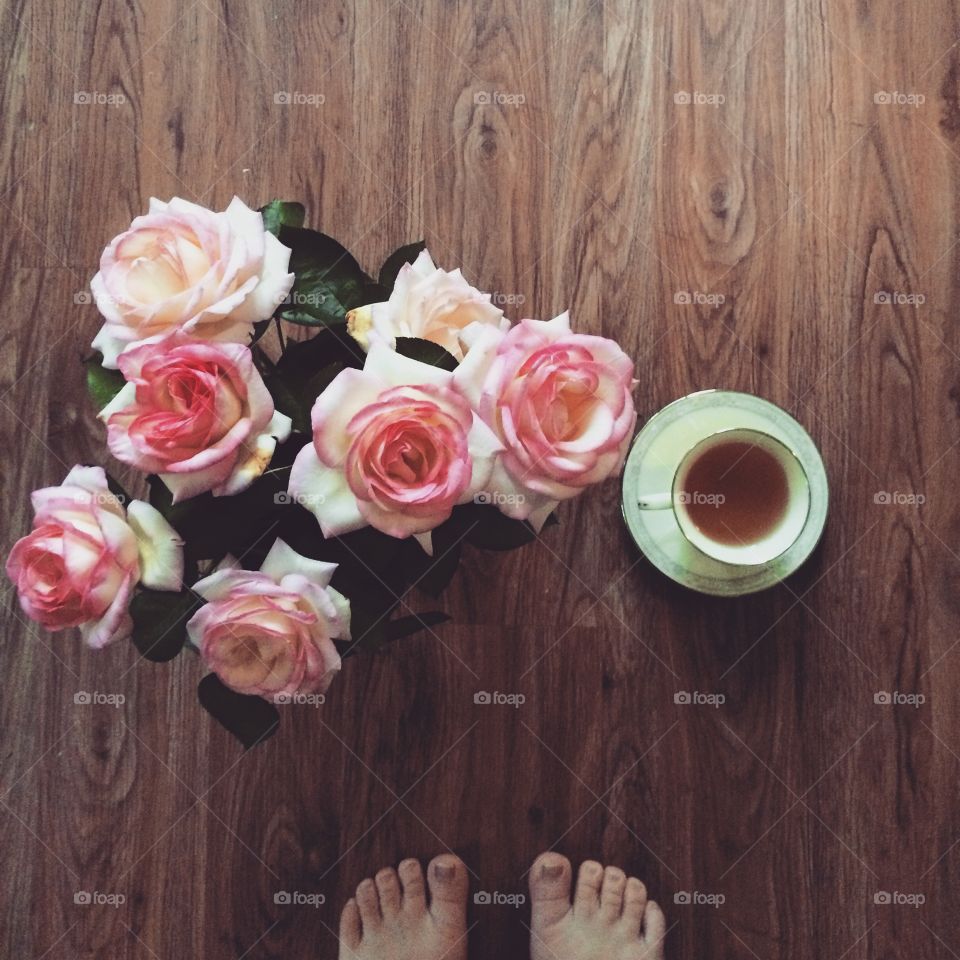 A bouquet of pink roses, a hot cup of tea, and bare feet on the wooden floor. A cozy still-life. 