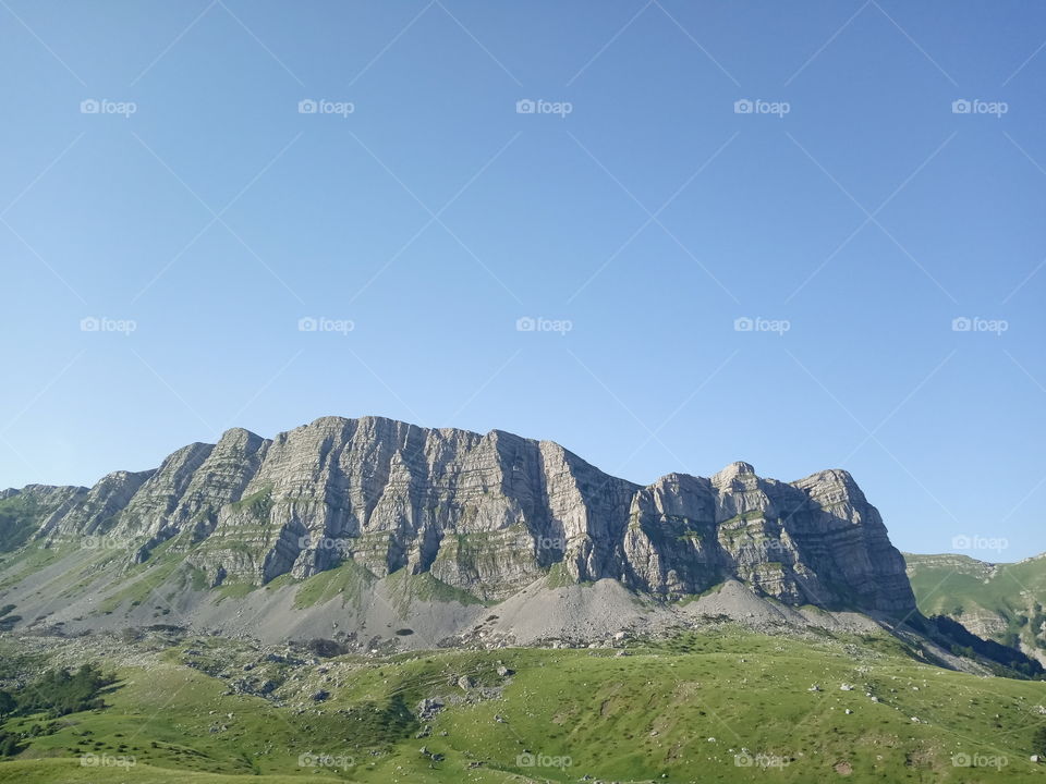 High rock raising from natural green meadow in to the clear blue sky. Volujak mountain, Dinarides mountain range, Balkan peninsula, South East Europe.