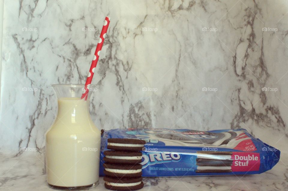 Oreo double stuff cookies stack next to a carafe of milk on a marble backdrop with a red and white straw