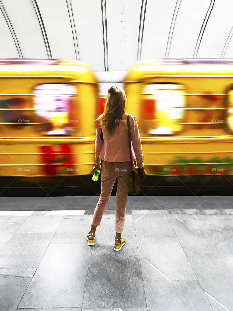 Young woman standing in front of moving yellow train in subway 