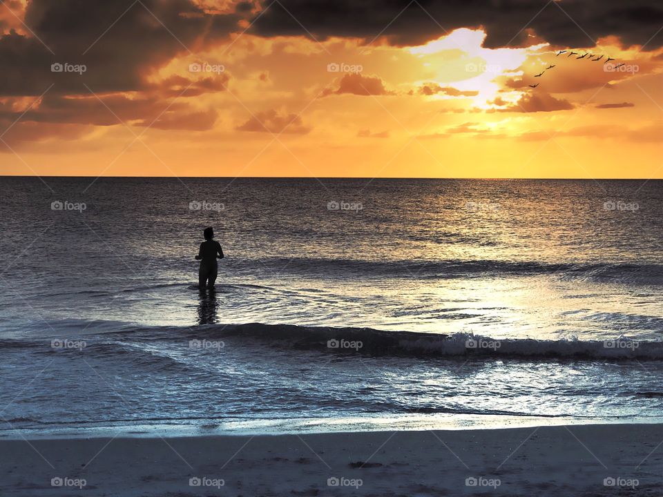 Woman wading in the ocean under a dark and beautiful sunset.