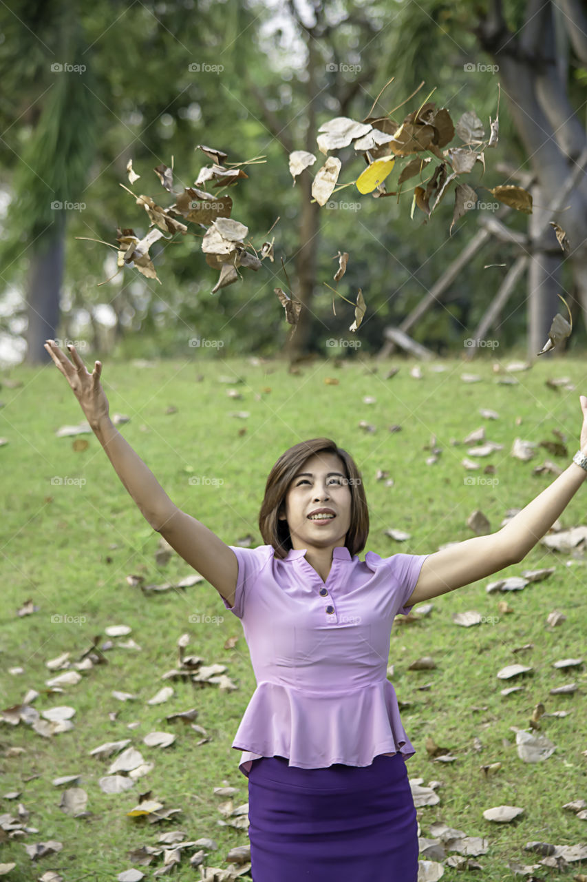 Portrait of Asean woman throwing dry leaves on the lawn in a park.