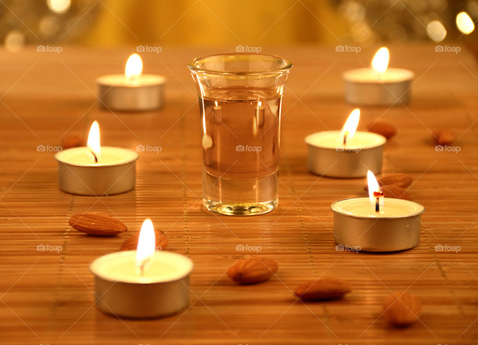 Almond oil in a glass between candles and almonds in the bathroom