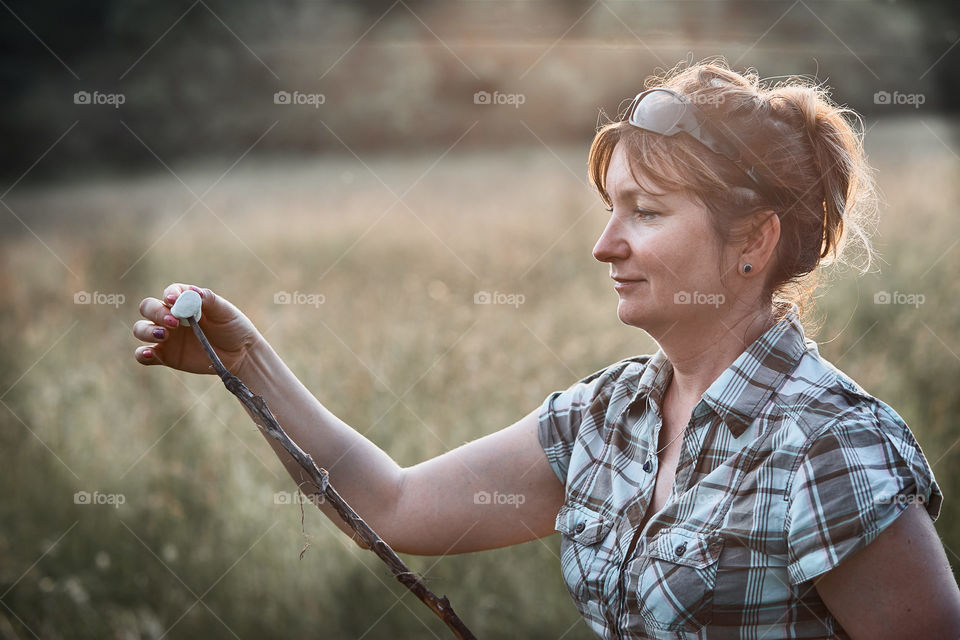 Woman roasting a marshmallows over a campfire on meadow. Vacations close to nature. Candid people, real moments, authentic situations