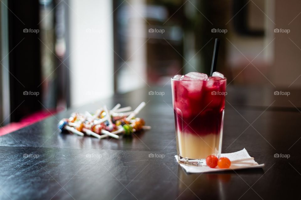 Cherry-banana juice with ice cubes and lollipops on wooden table