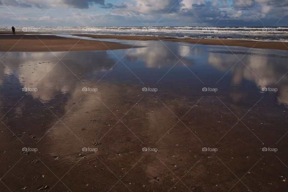Clouds reflection in the water on the beach, sunny day with clouds, near the sea