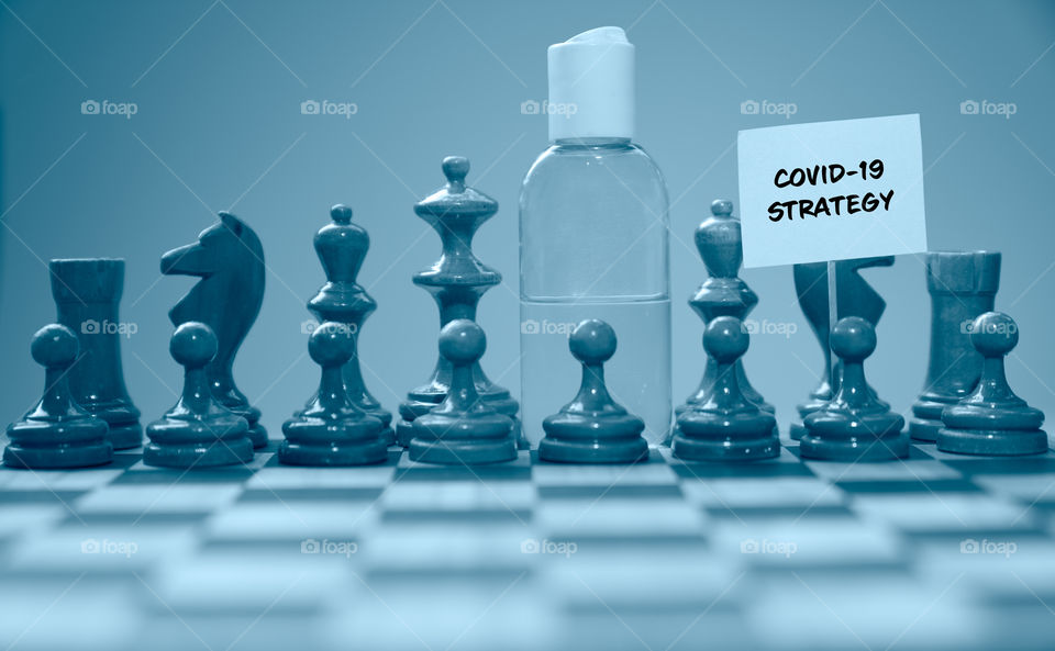 Coronavirus concept image chess pieces and hand sanitizer on chessboard illustrating global struggle against novel covid-19 outbreak.