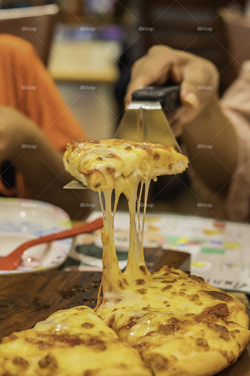 The hand holding Pizza with ham and cheese in spoon from the tray wood.