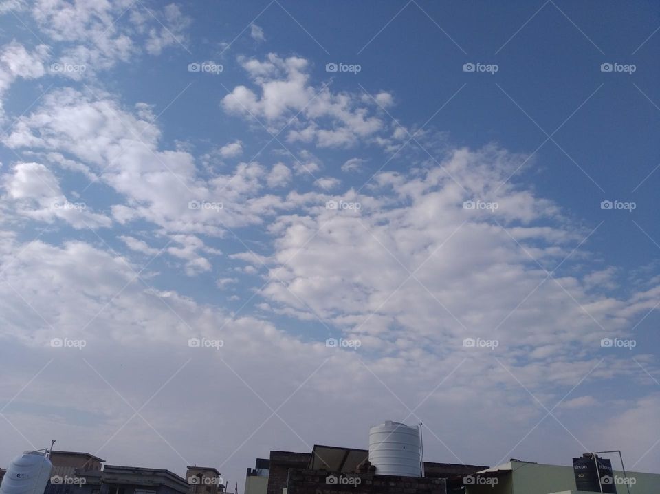 a shiney day white clouds in blue sky whitish cloud scattered dark tree looks very beautiful