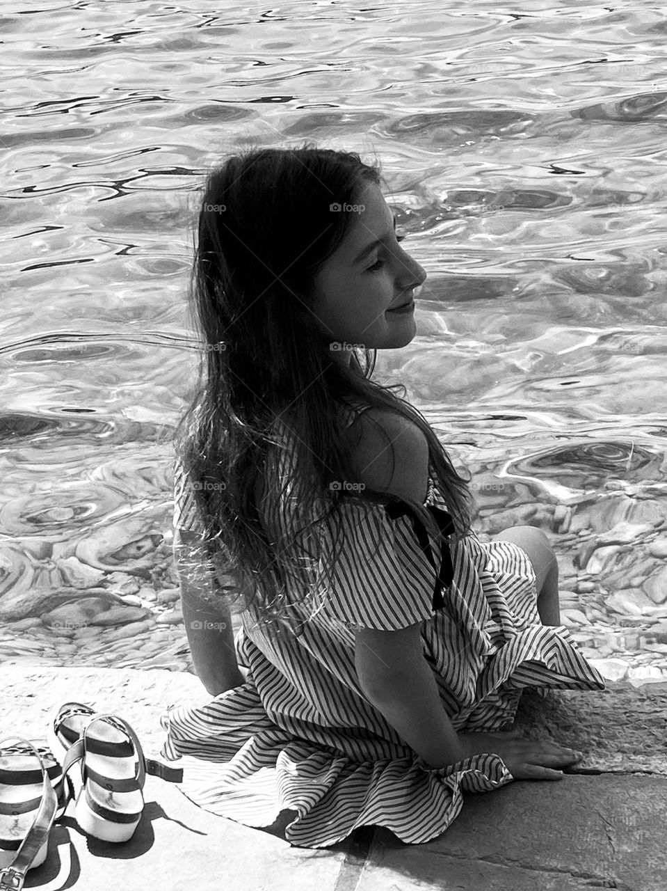 Black and white picture of a girl looking out peacefully while putting her feet in the water.