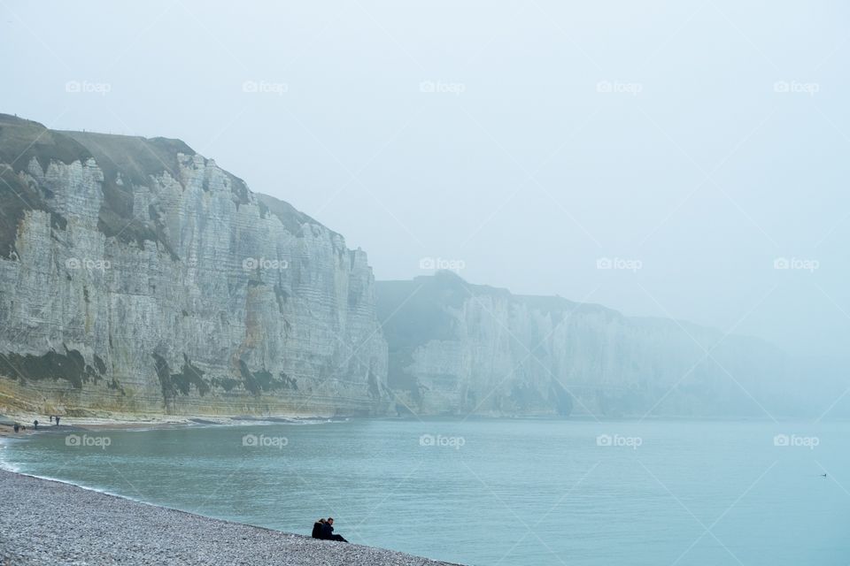 Silhouette of a couple watching over the fading sea from the Foggy beach of Fécamp, Normandy, France with the white chalk cliffs in the background