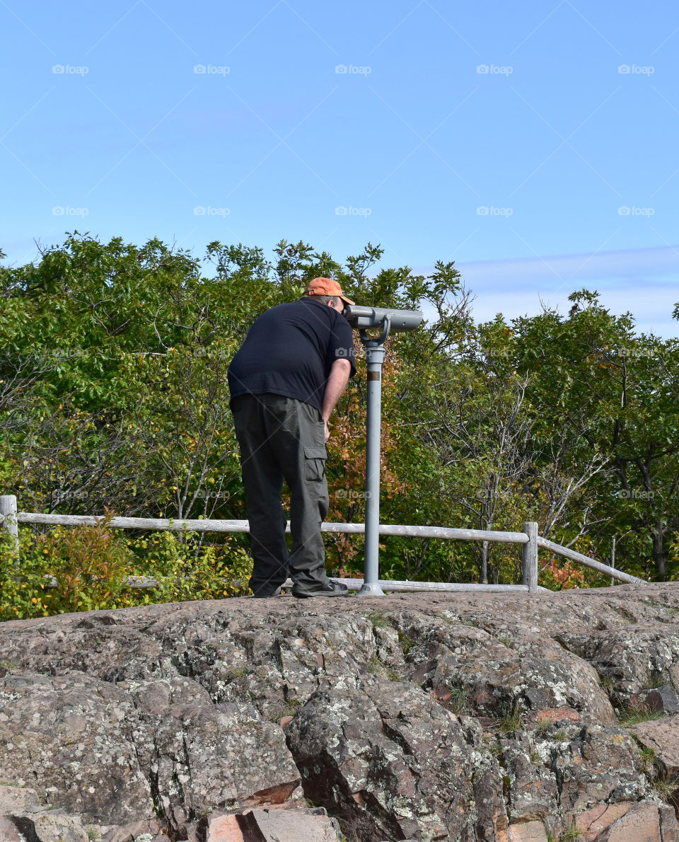 Man in a scenic overlook using a telescope