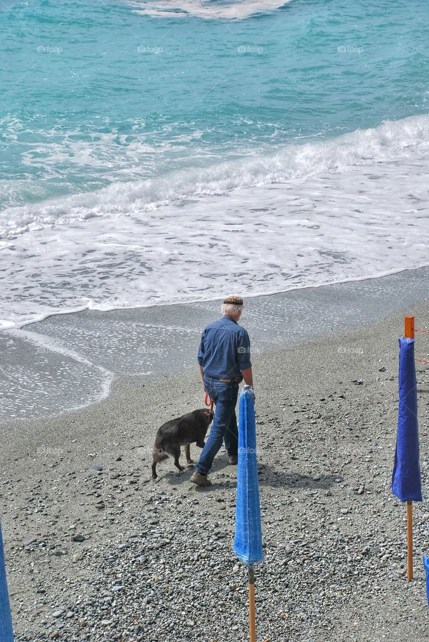 Beach pals. A man and his dog walk along the empty beach as waves hit the shore