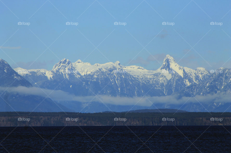 Another rare but welcome sunny winter day in Beautiful British Columbia. This shot is the Mainland mountains viewed from Vancouver Island. There is a wisp of clouds over the foothills and the dark blue ocean of the Salish Sea in the foreground.